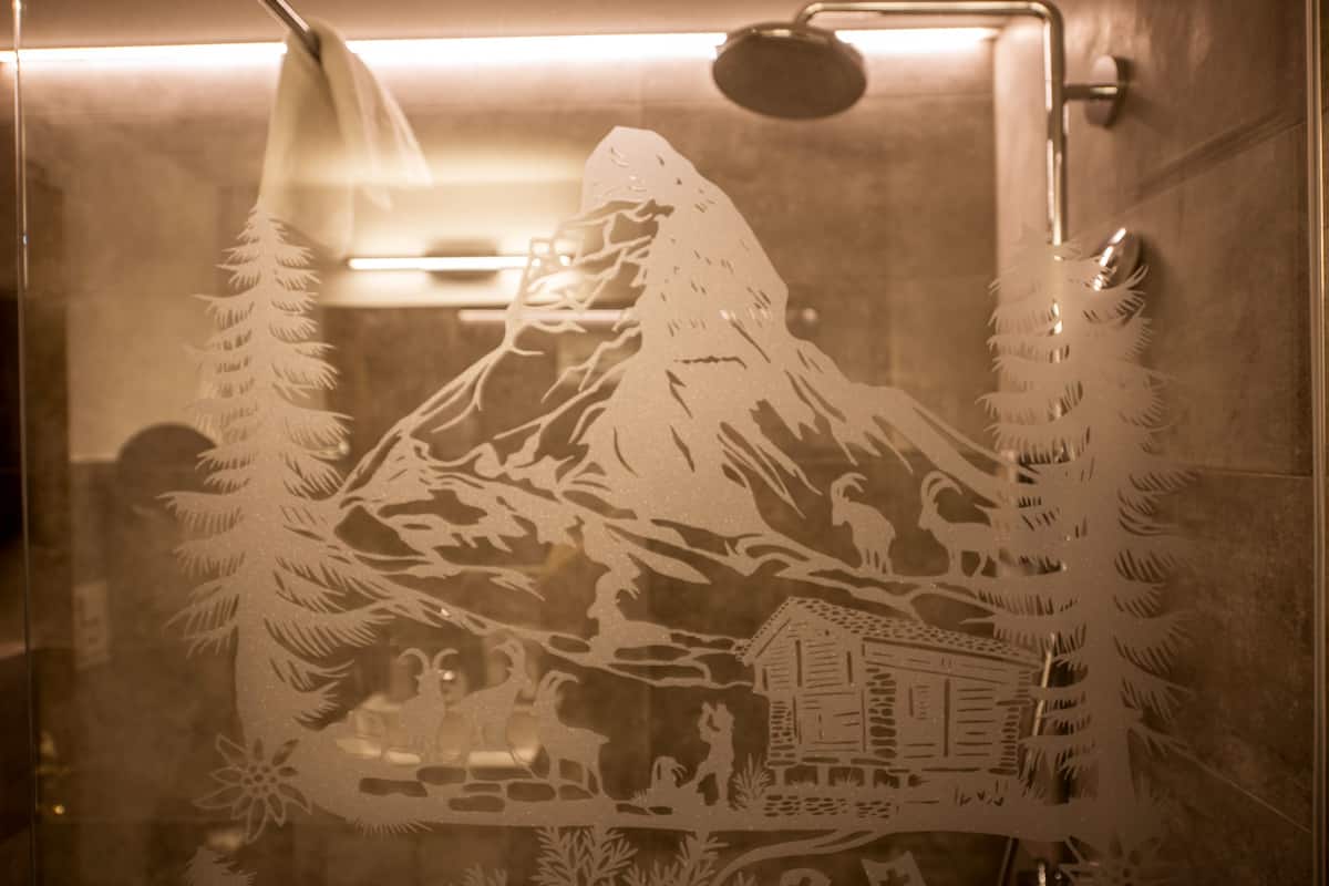 A frosted glass window with a mountain scene, including a cabin and trees.