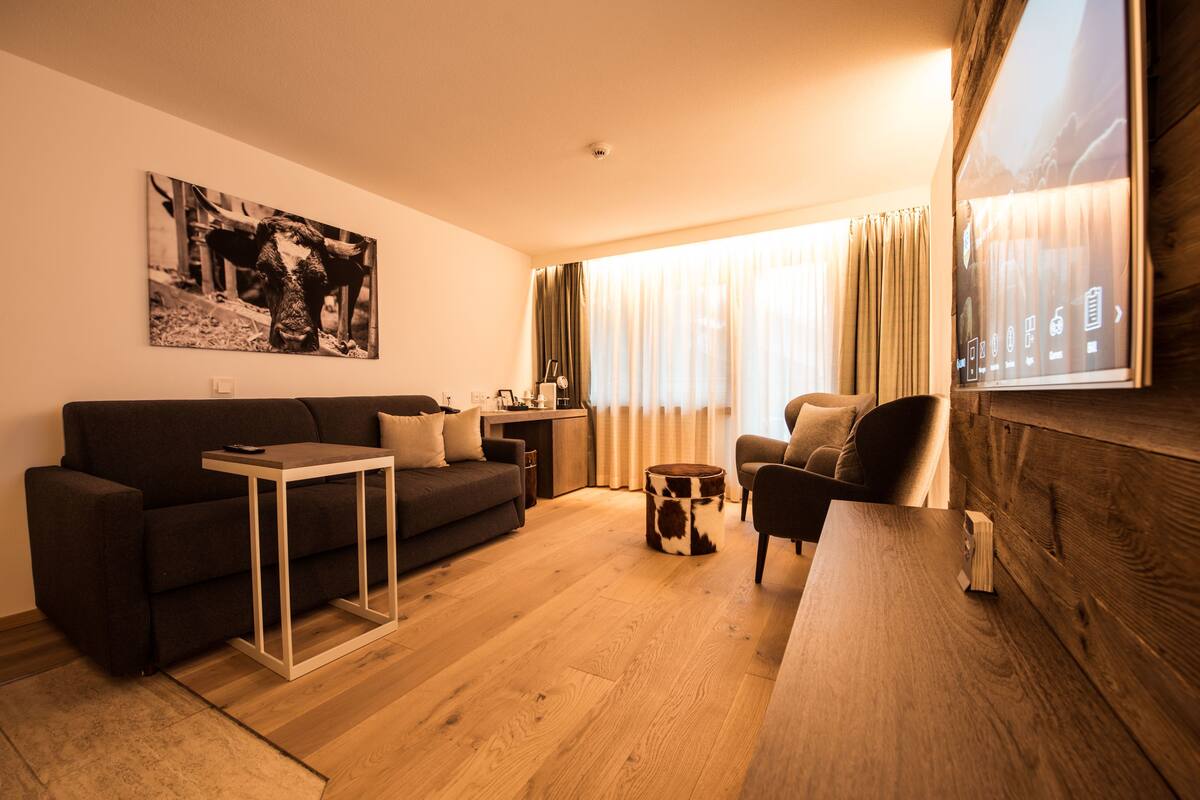 A modern living room with a dark sofa, a small coffee table, a wooden side table, and a large window with curtains.