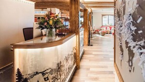 A reception area with a wooden reception desk, a vase with flowers, and a sign for 'NESPRESSO'. - Hotel Daniela (Zermatt)