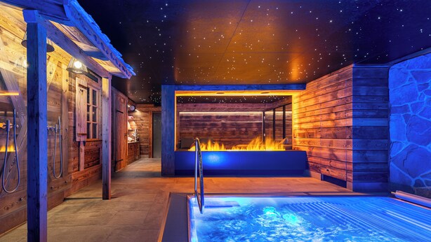 A spa area with a hot tub, wooden walls, and a fire feature. - Hotel Daniela (Zermatt)