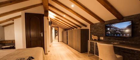 Una moderna camera d'hotel con soffitto in legno, un letto con un logo, una scrivania con una sedia e una TV che mostra un messaggio di benvenuto.