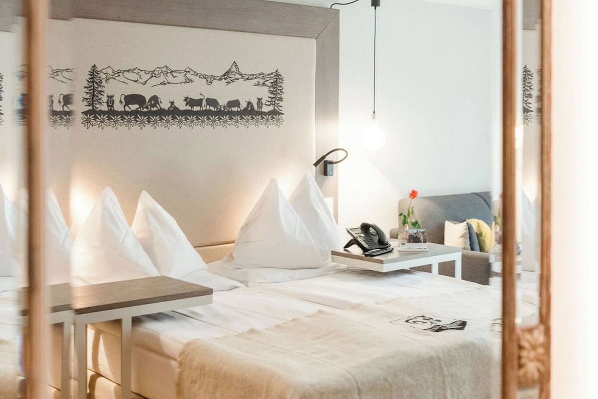 A modern hotel room with a large bed, bedside tables, a mirror, and a wall-mounted artwork.