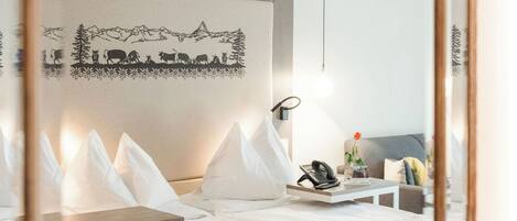 A modern hotel room with a large bed, bedside tables, a mirror, and a wall-mounted artwork.