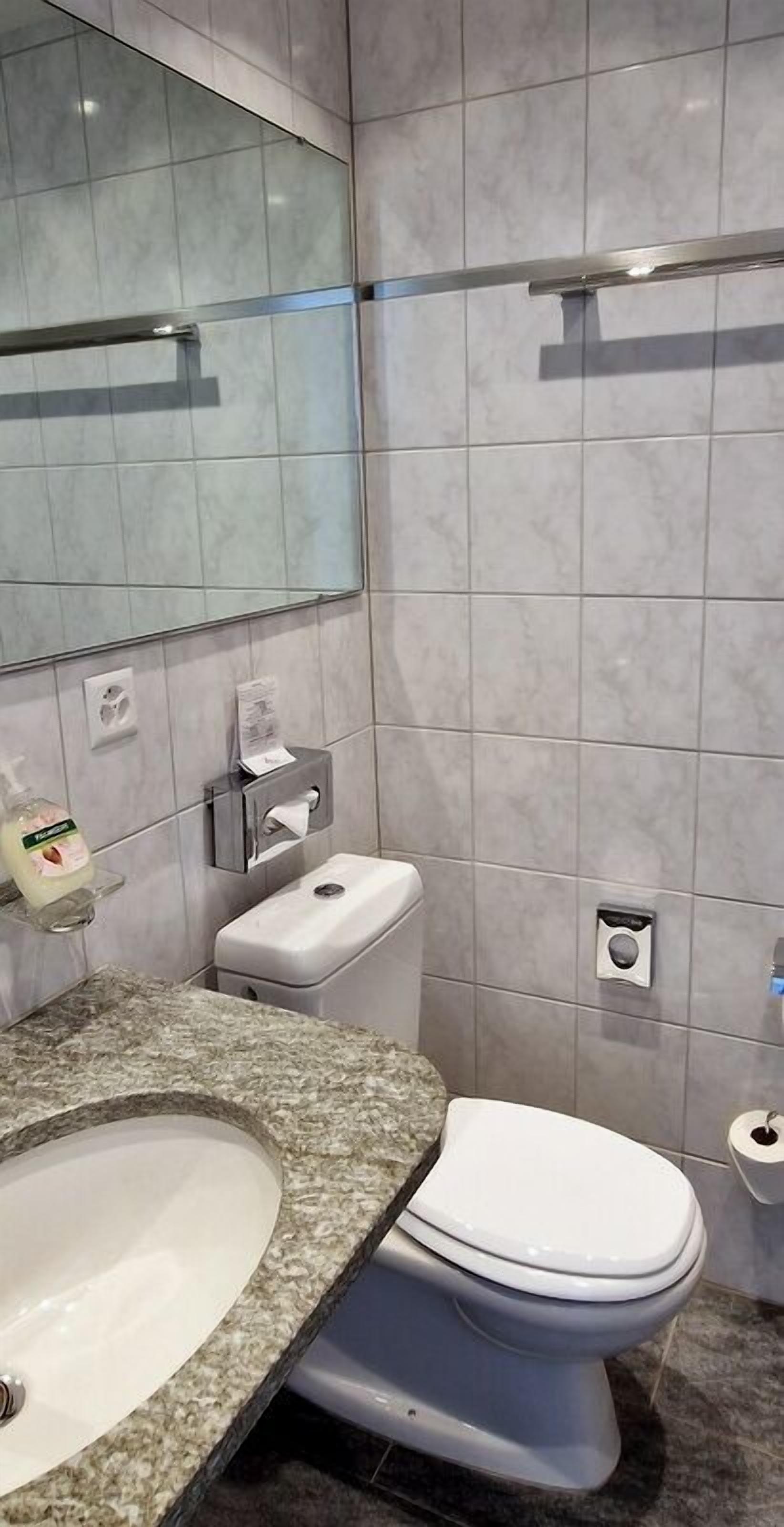 Une salle de bain moderne avec un comptoir en granit, un lavabo blanc, des toilettes et un miroir.