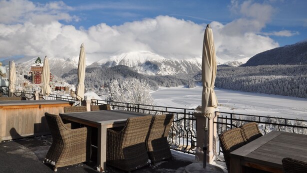 Eine Terrasse mit Korbmöbeln und Sonnenschirmen mit Blick auf eine verschneite Berglandschaft.