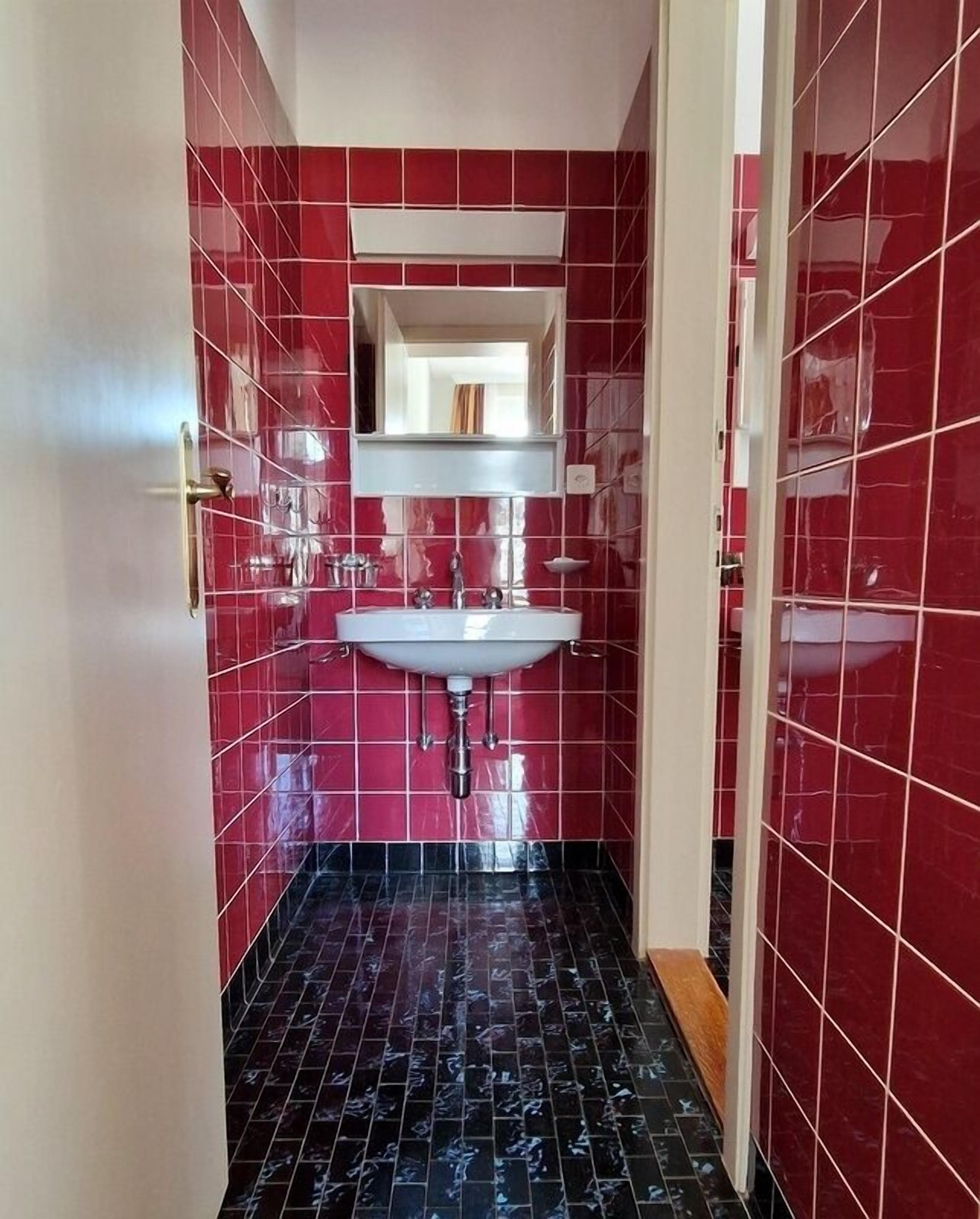 Un baño estrecho con paredes de baldosas rojas y suelo de baldosas negras.
