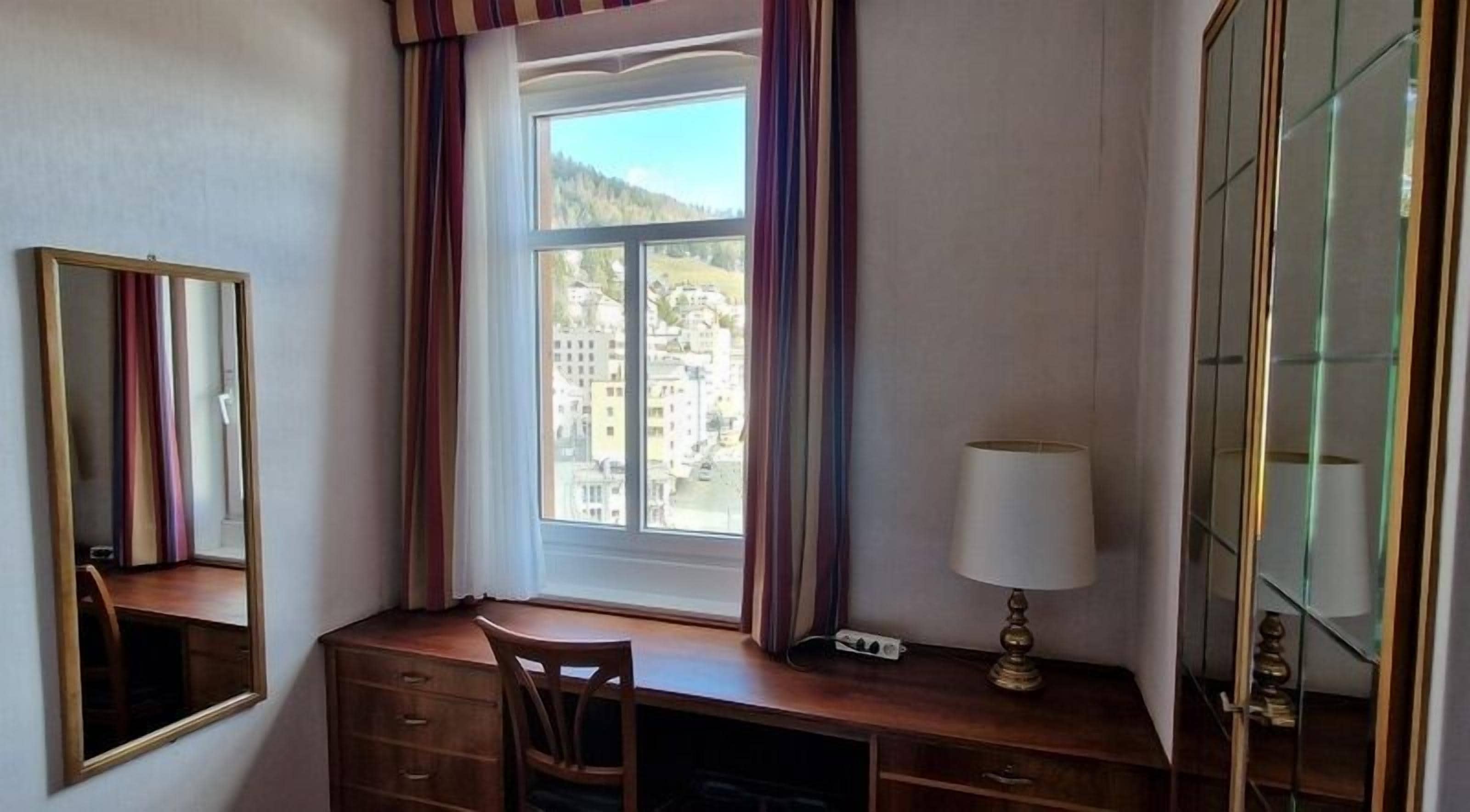 A room with a desk, chair, and a large window with curtains.