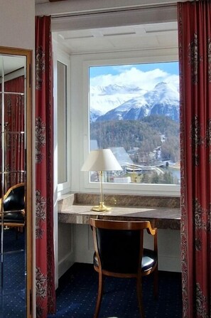 A hotel room with a desk, chair, and a large window offering a mountain view.