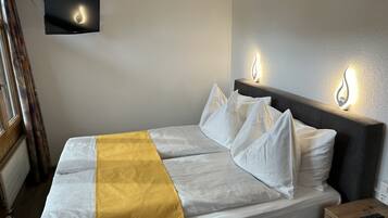 A neatly made bed with white and yellow bedding, a flat-screen TV mounted on the wall, and bedside lamps.