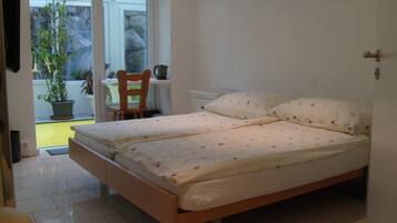Un dormitorio con una cama, una silla y una mesita. Se ve un jardín desde la ventana.