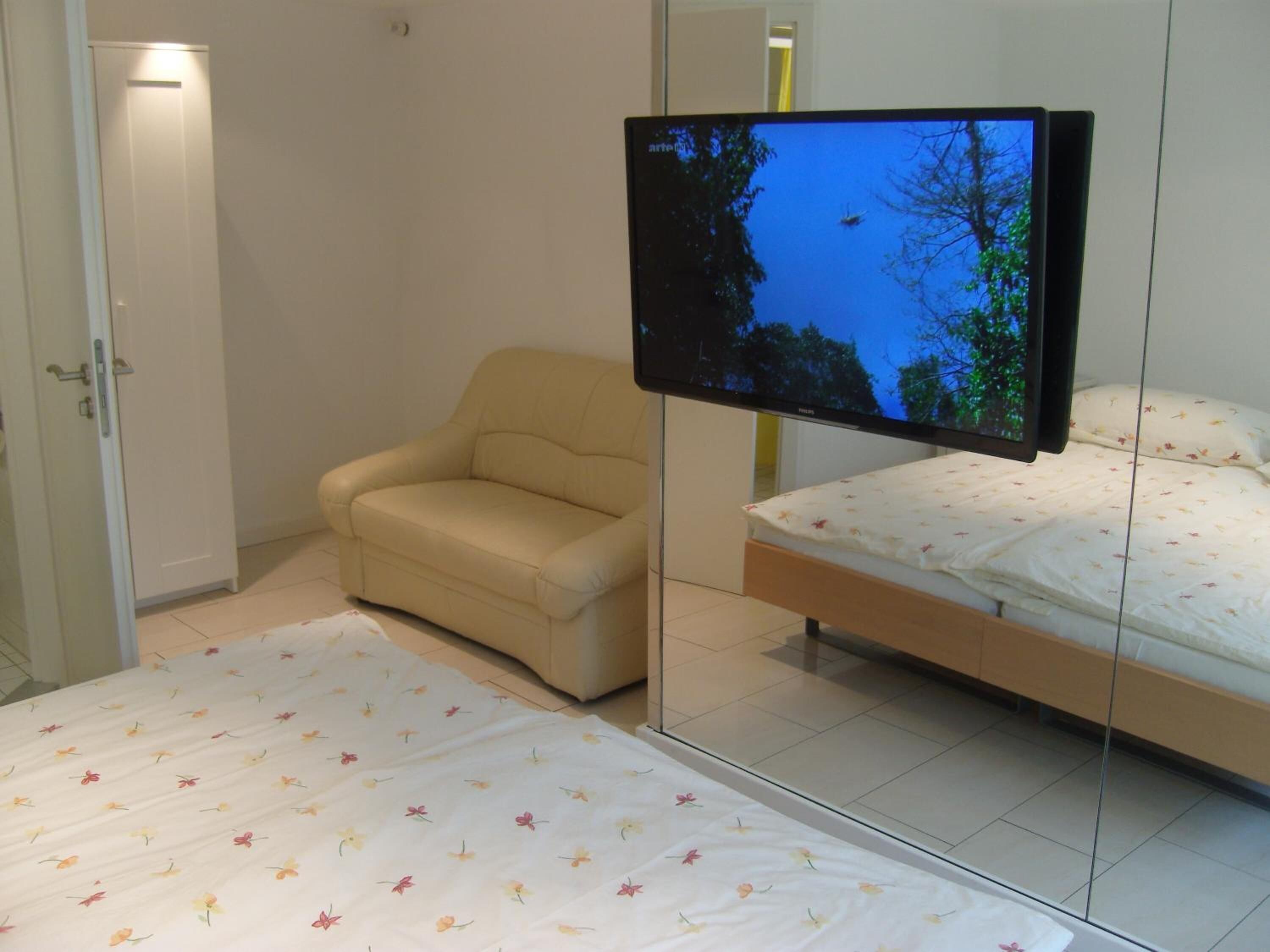 Une chambre à coucher avec un lit, un canapé et un téléviseur fixé au mur.
