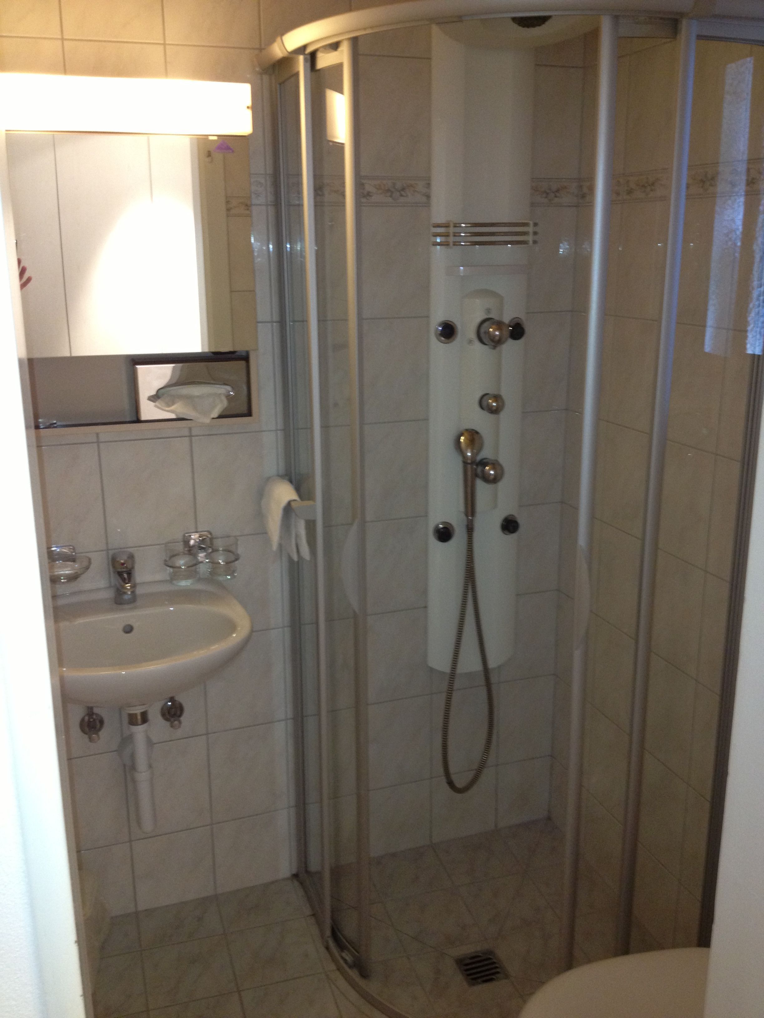 Une petite cabine de douche fermée, dotée d’une porte en verre, d’un lavabo et d’un miroir placé au-dessus.