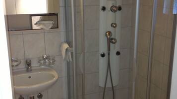 Une petite cabine de douche fermée, dotée d’une porte en verre, d’un lavabo et d’un miroir placé au-dessus.