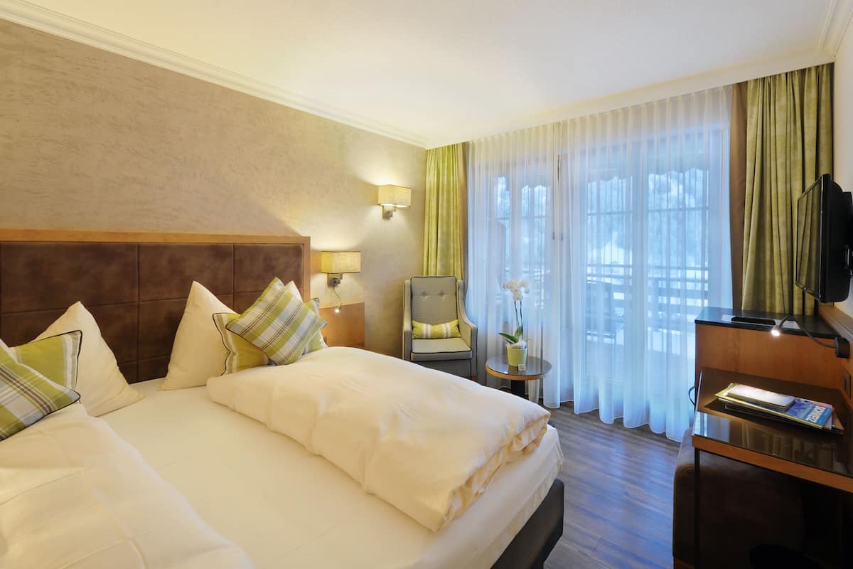 A hotel room with a large bed, a chair, a desk, a television, and a window with curtains.