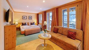 A hotel room with a bed, a sofa, a small table with a vase, wooden walls, and large windows. - Hotel Kirchbuehl (Grindelwald)