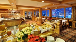 A buffet area with various food items and a view of a snowy landscape through large windows. - Hotel Kirchbuehl (Grindelwald)