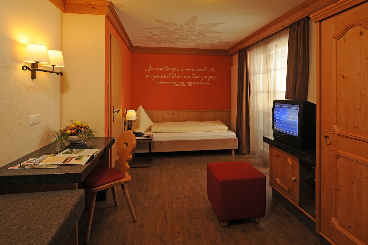 A hotel room with a bed, a desk with a chair, a television, and a wooden cabinet.