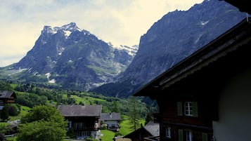 A mountain village with traditional wooden houses, a clear view of a prominent mountain peak, and a lush green valley.