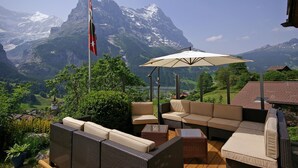 An outdoor seating area with wicker furniture and a flagpole, overlooking a mountainous landscape. - Hotel Kirchbuehl (Grindelwald)