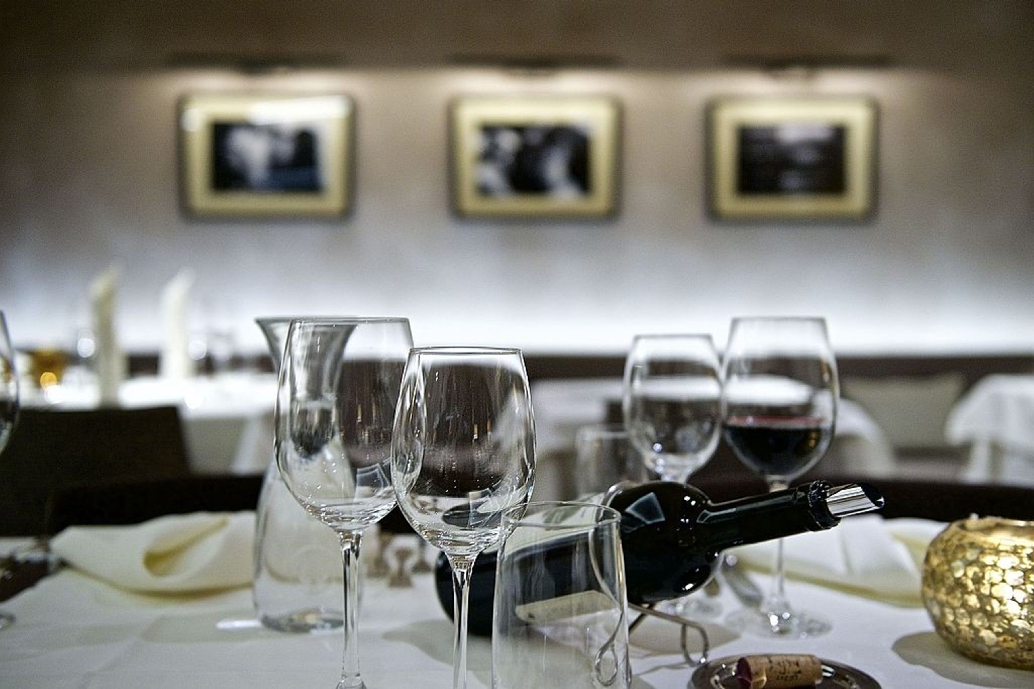 A table with wine glasses and a bottle, set in a dining area with framed pictures on the wall.