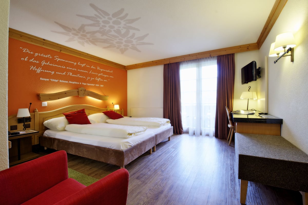 A hotel room with a large bed, two bedside tables, a desk with a chair, a TV, and a window with curtains.