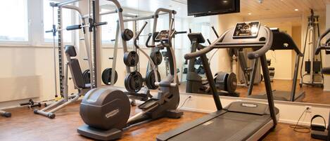 A gym with cardio equipment, weight machines, and a TV mounted on the wall.