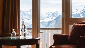 A room with a view of snow-covered mountains, a glass table with bottles, and a brown leather chair. - Hotel Silberhorn - Residences & Spa Wengen (Lauterbrunnen)