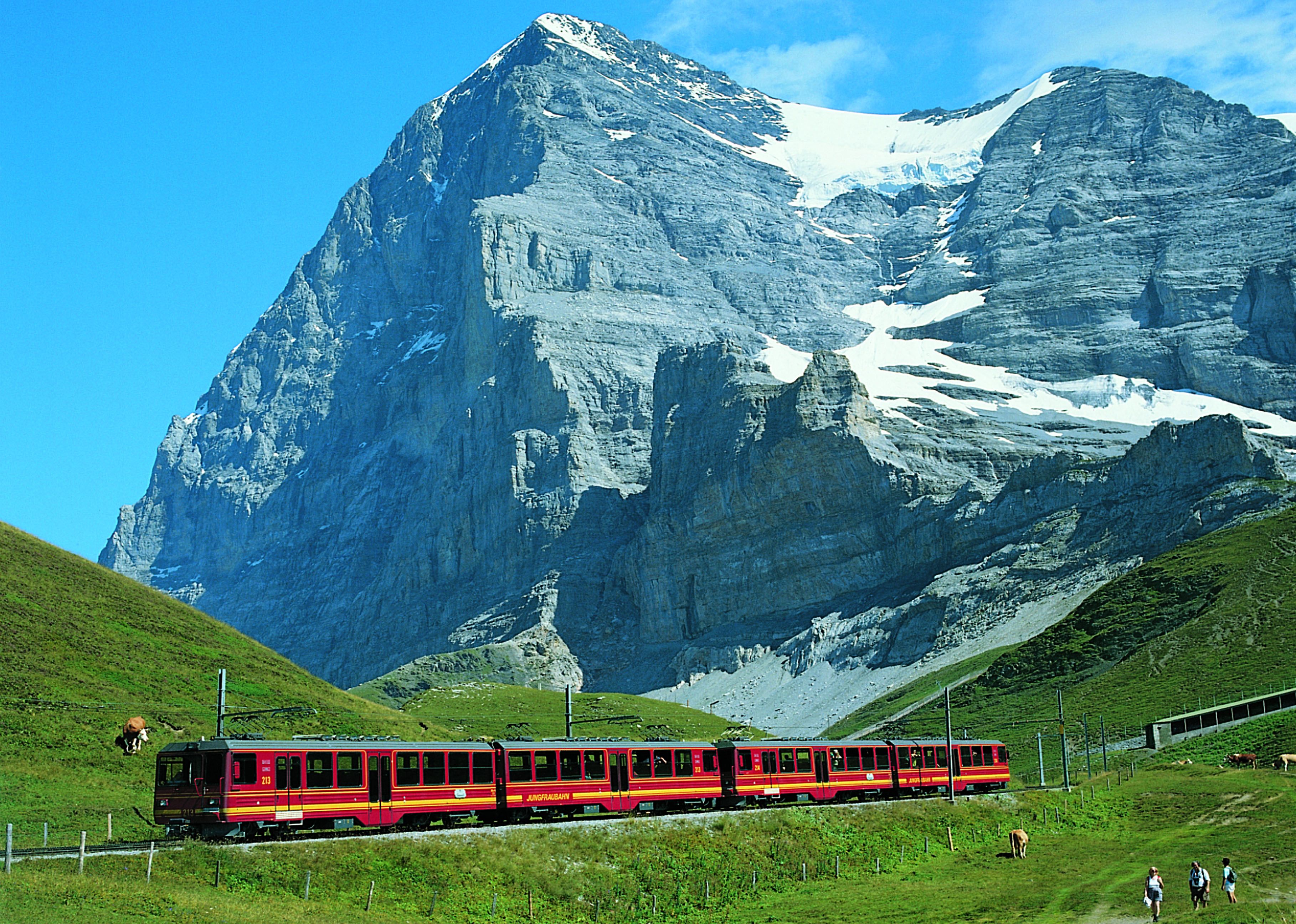Un tren rojo sobre rieles, con montañas al fondo.