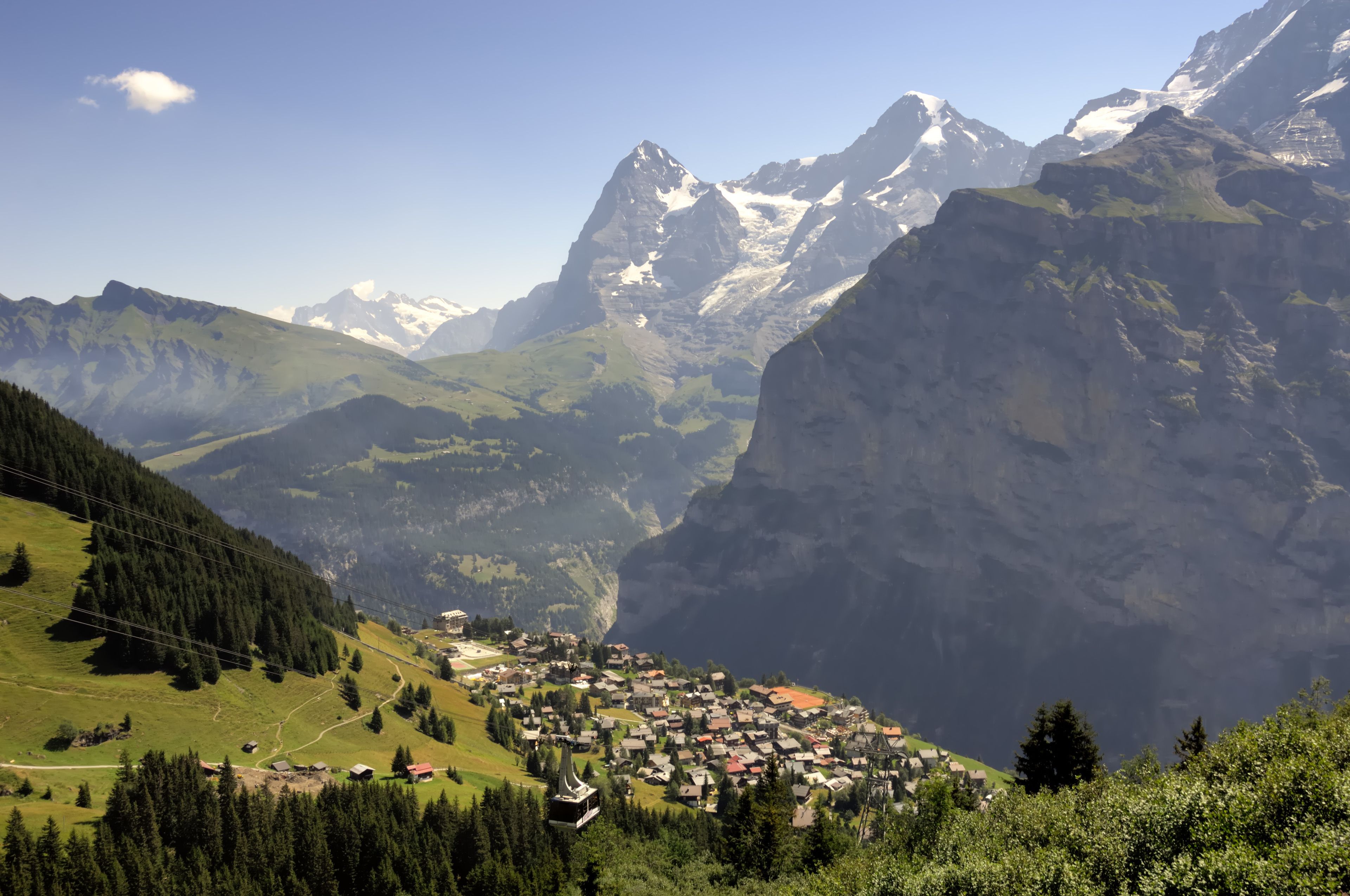 A mountain village with houses and a ski lift, surrounded by steep, snow-capped mountains.
