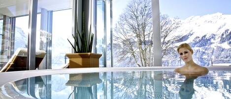 Una piscina interior moderna con vistas despejadas a montañas nevadas.