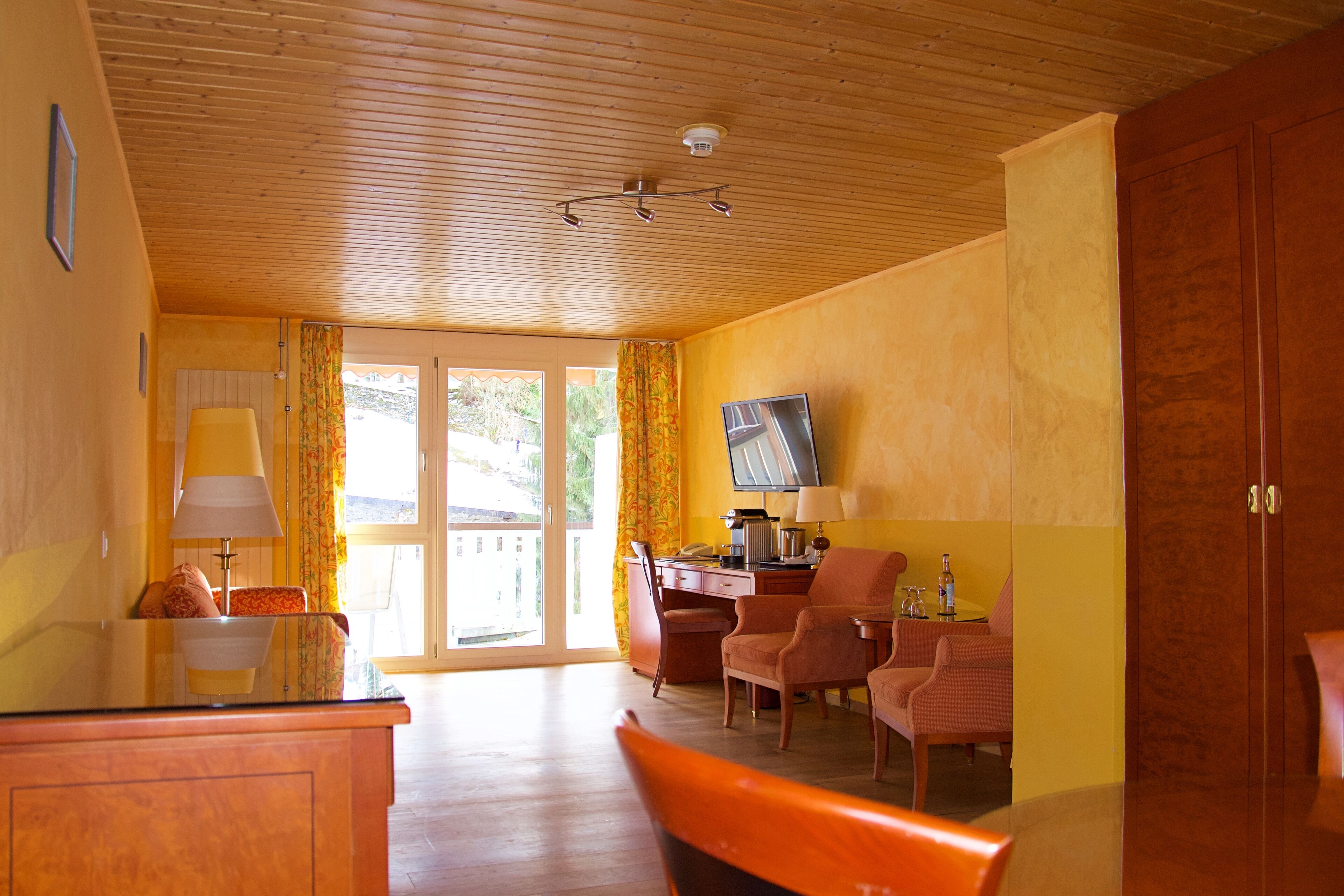Une pièce avec un plafond en bois, un téléviseur fixé au mur, un bureau avec une chaise et un canapé.