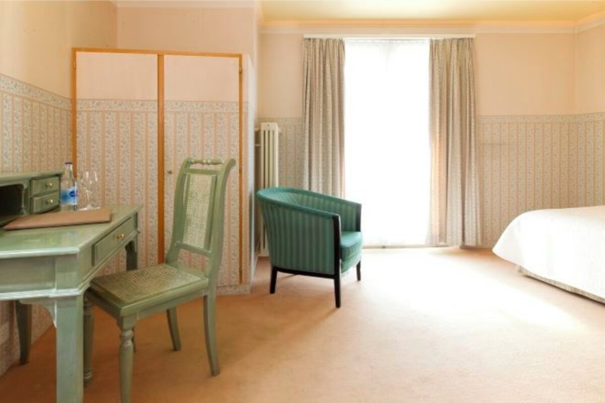 Een hotelkamer met een bed, een bureau met stoel, een radiator en een raam met gordijnen.