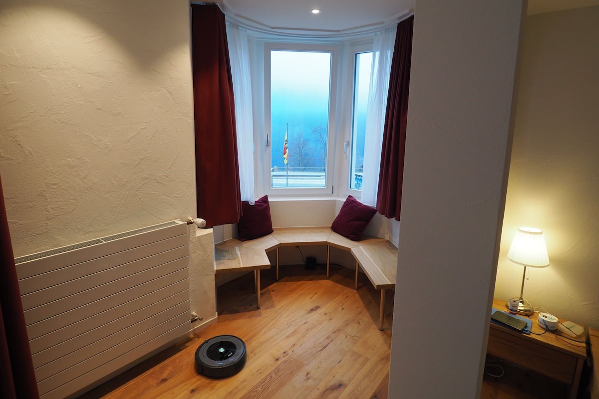 Une petite pièce avec une fenêtre, un radiateur, un bureau et une lampe.