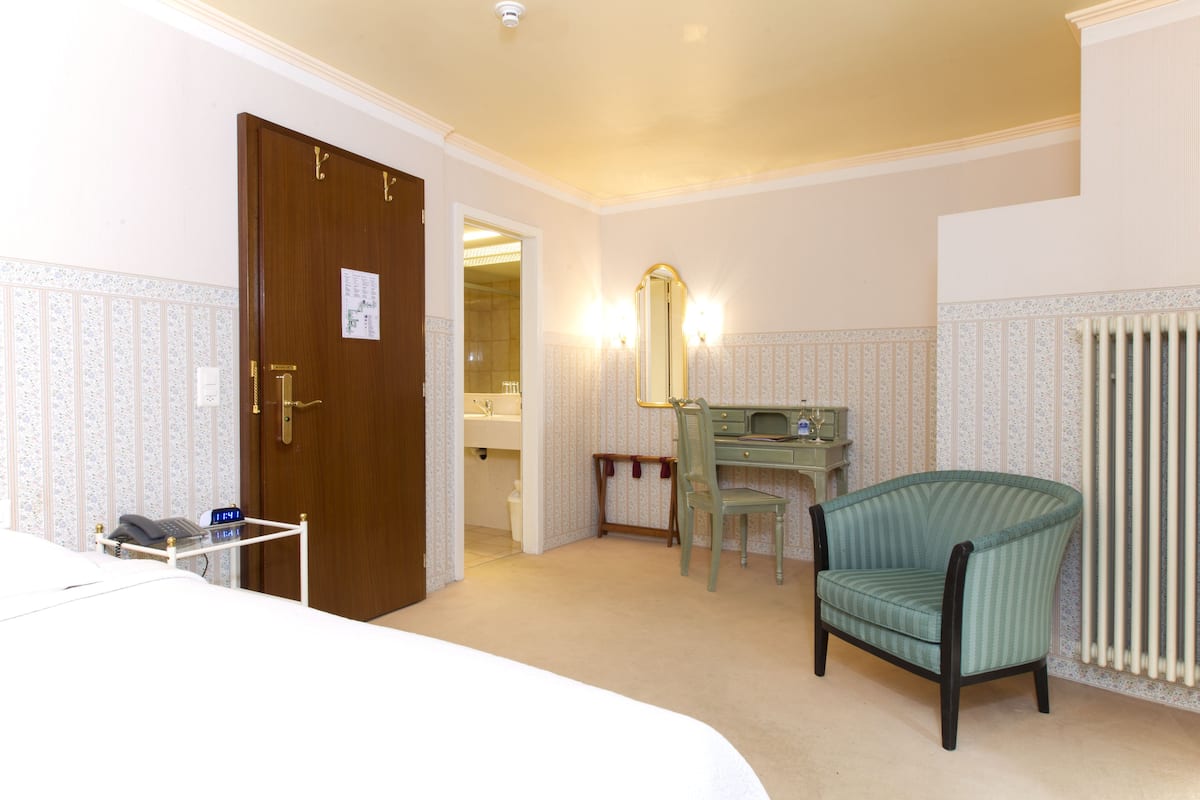 Une chambre d’hôtel avec un lit, un bureau et une chaise, un miroir et un radiateur.