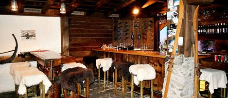 Un rústico espacio de bar con mobiliario de madera, suelo de piedra y una columna de piedra.