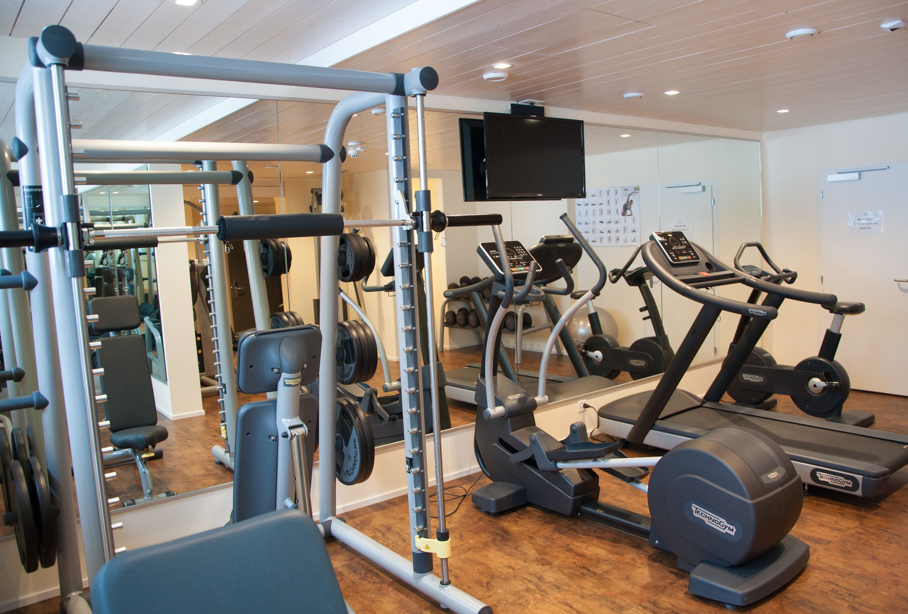A gym with exercise equipment, a television, and a mirror.