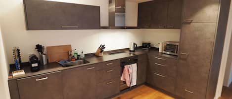 Una cocina moderna con armarios oscuros, encimera de madera y pileta de acero inoxidable.