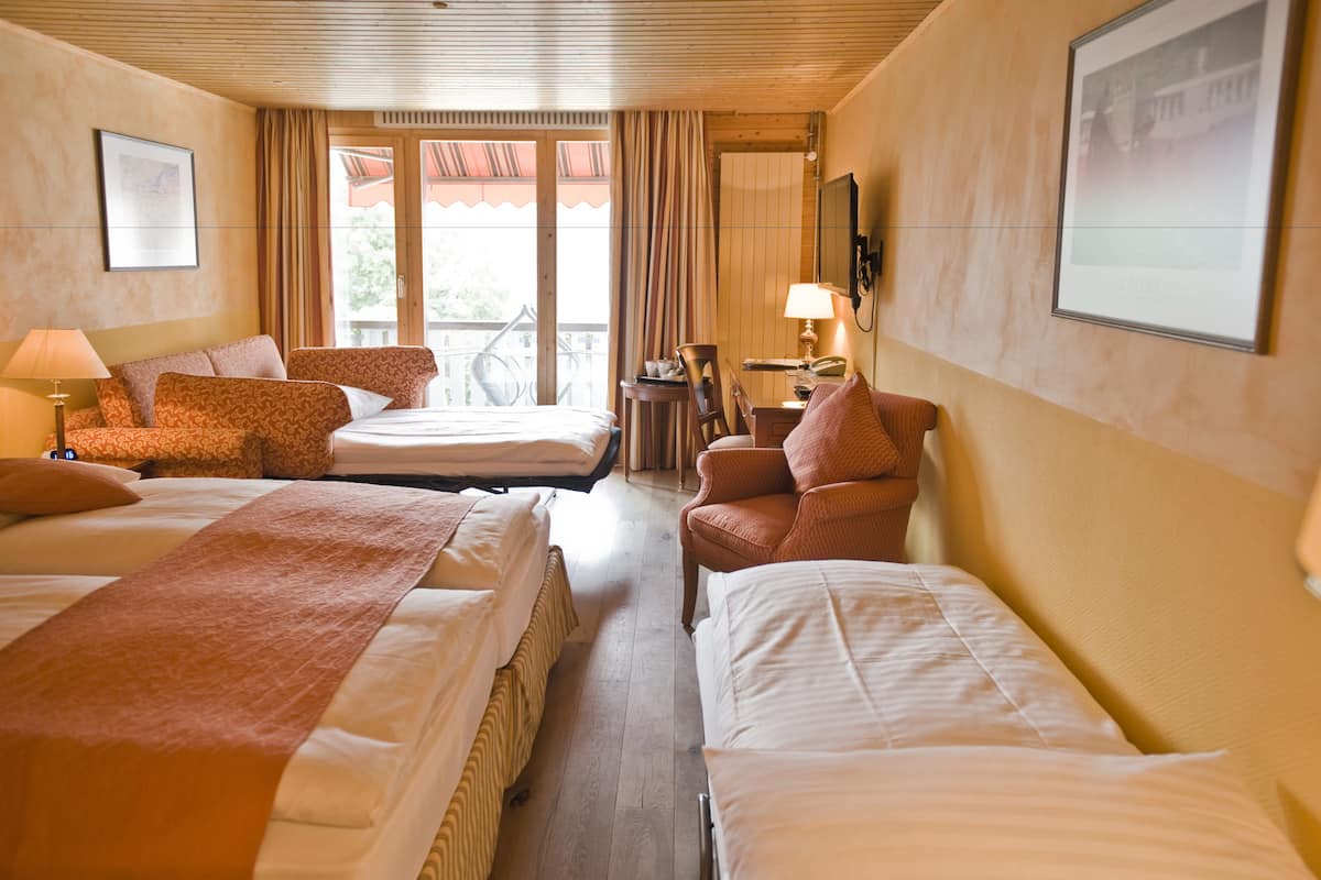 Une chambre d’hôtel avec deux lits, une chaise, un bureau, une lampe et un vélo visible à travers la fenêtre.