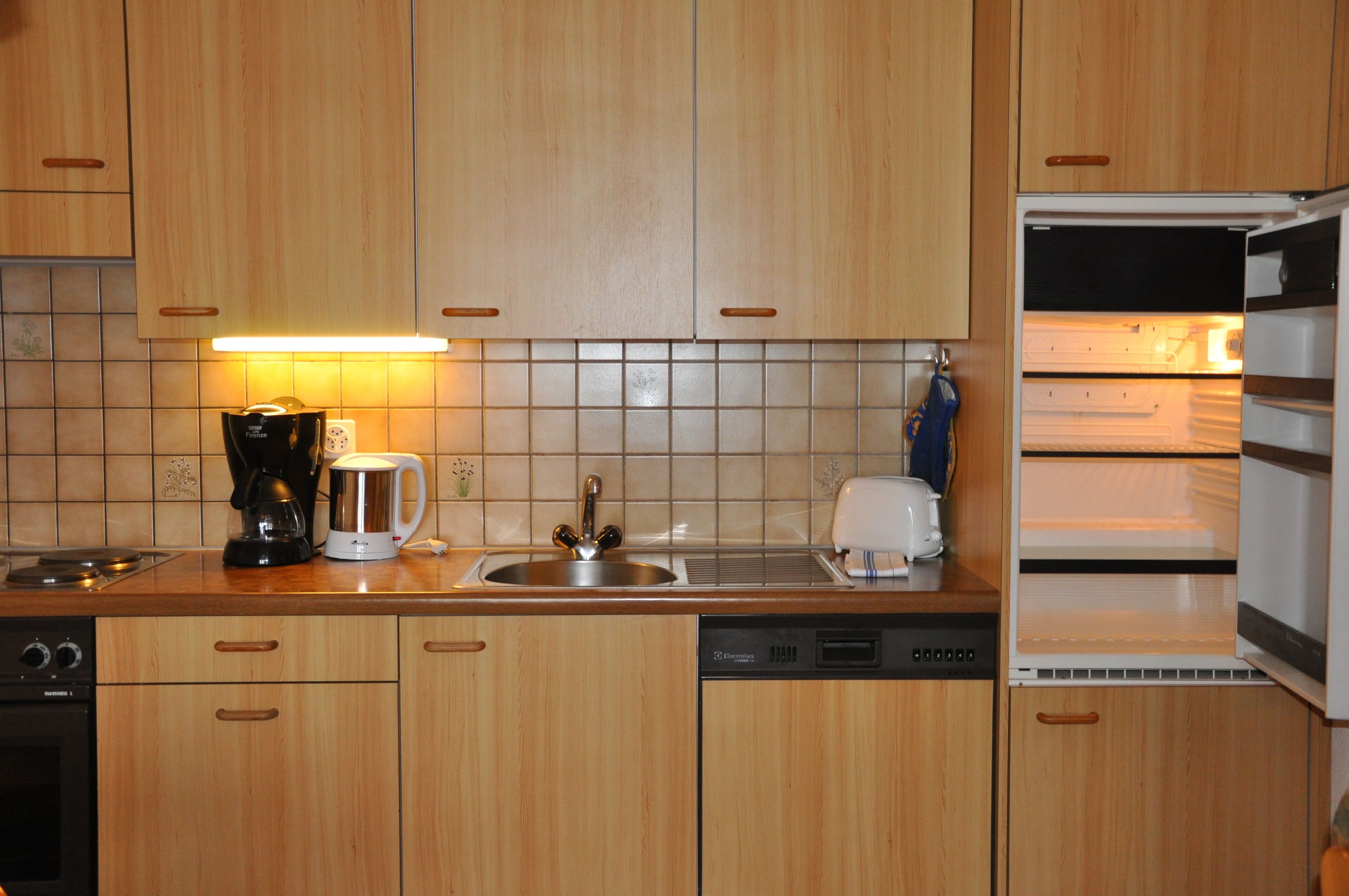 Una cocina con armarios de madera, cafetera, hervidor, tostadora y lavavajillas.