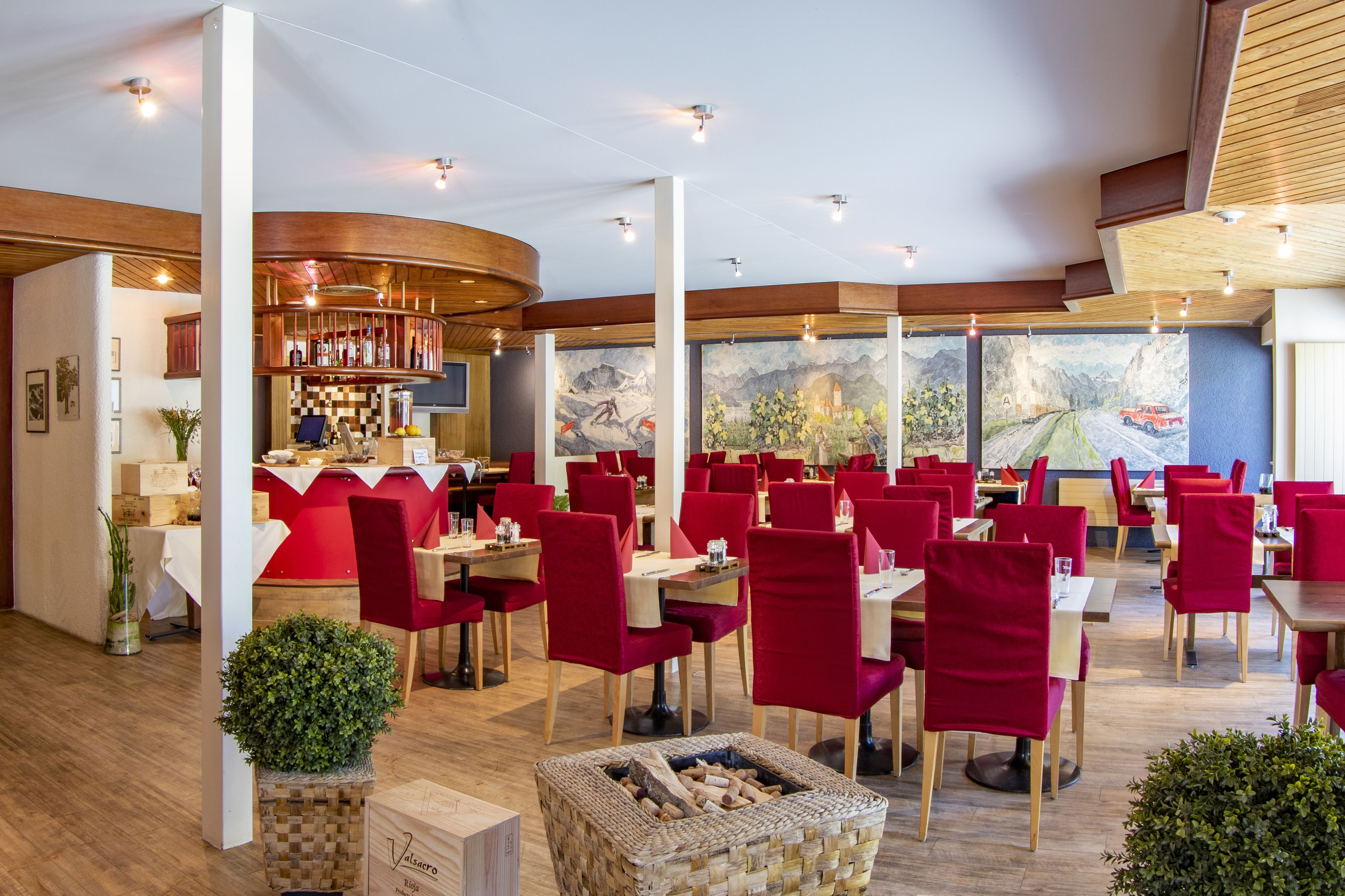 A restaurant with red chairs, wooden tables, and a view of a mountain landscape through large windows.