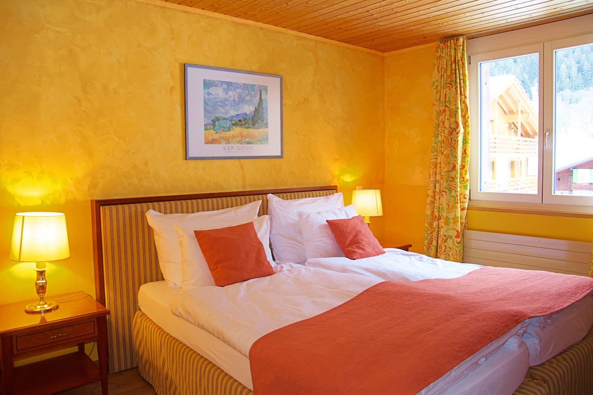 Une chambre d’hôtel avec un lit, deux lampes de chevet, un tableau encadré au mur et une fenêtre avec des rideaux.