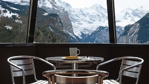 A dining area with a table and chairs, a cup, and a plate with a slice of cake, overlooking a mountainous landscape. - Hotel Silberhorn - Residences & Spa Wengen (Lauterbrunnen)