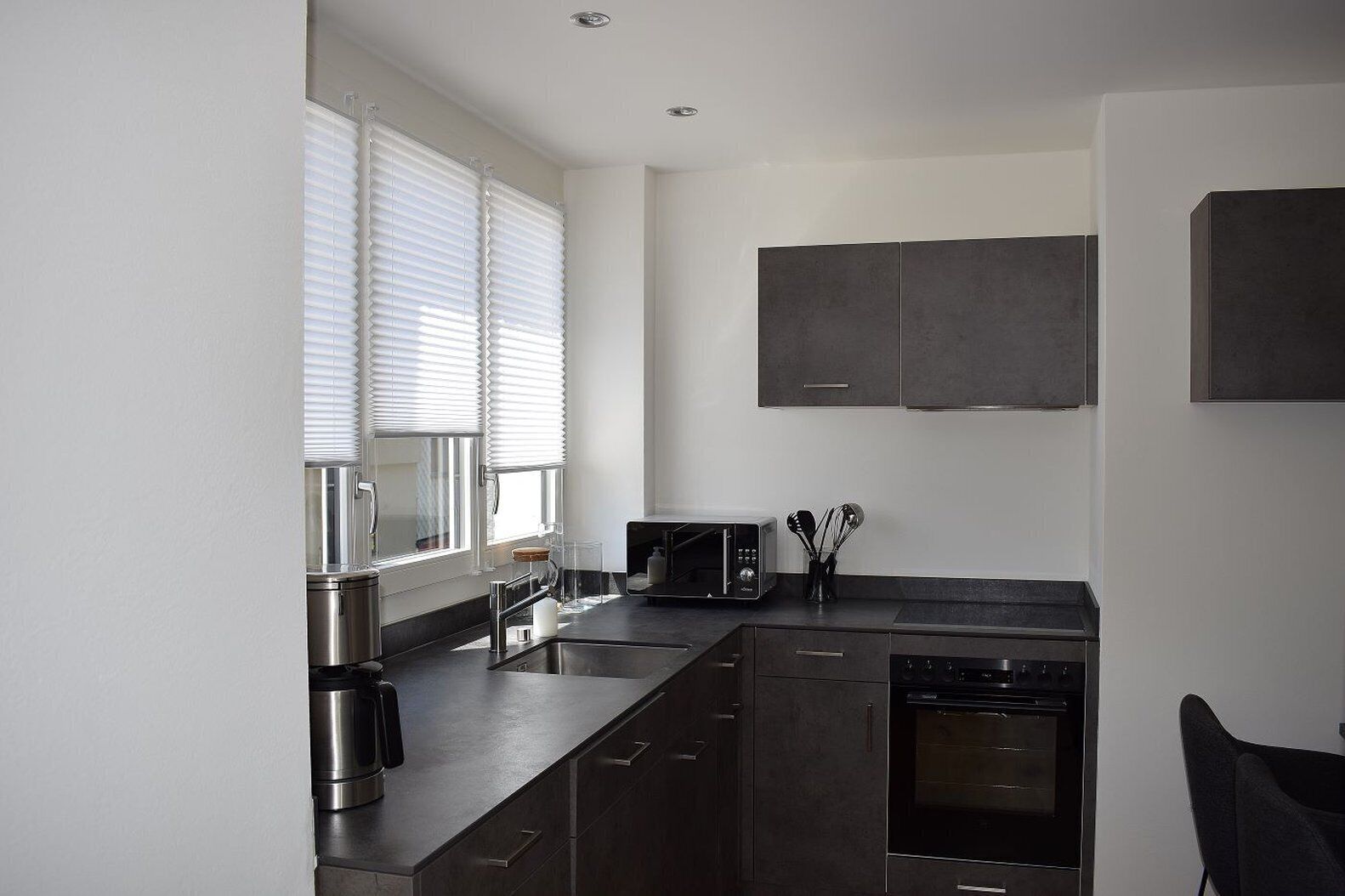 A modern kitchen with dark cabinets, a built-in oven, a coffee maker, and a microwave.