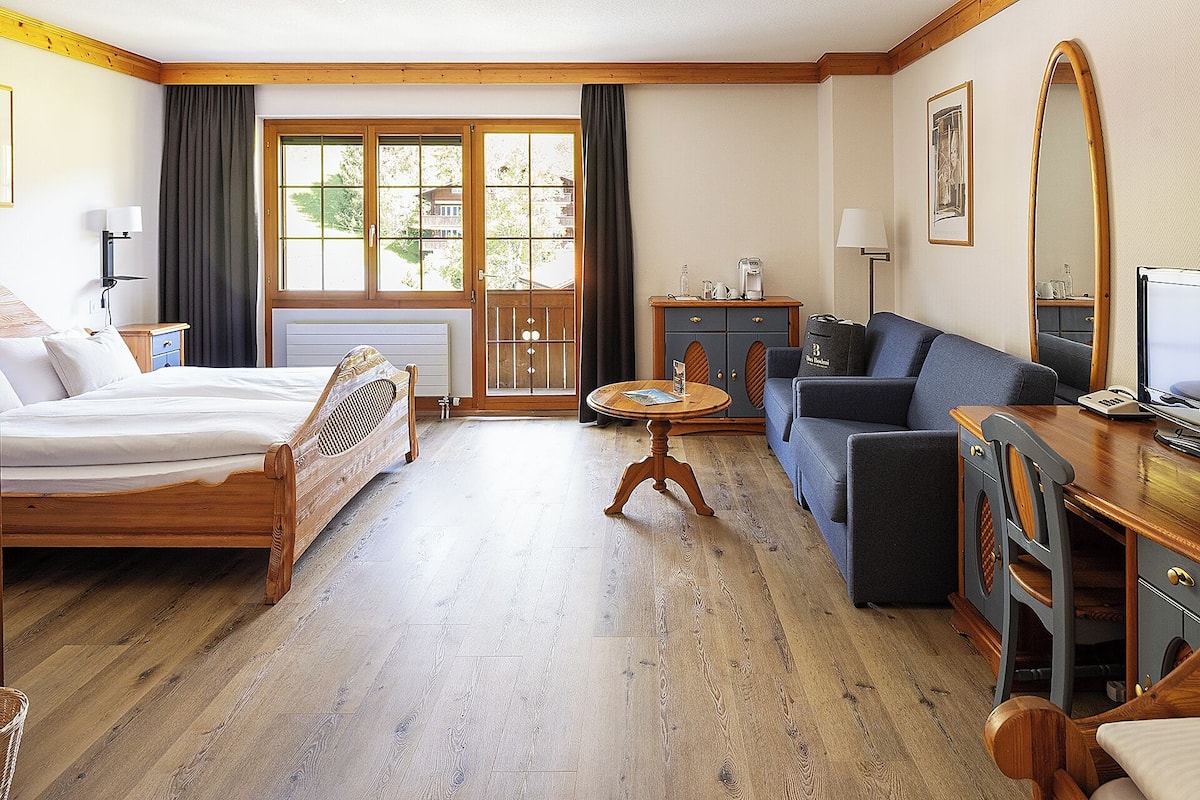 A hotel room with a bed, a sofa, a small table, a cabinet, and a window with curtains.