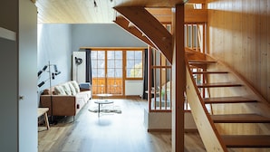 Amplia sala de estar con una escalera de madera, un sofá, una mesa de centro y vistas a través de grandes ventanales.