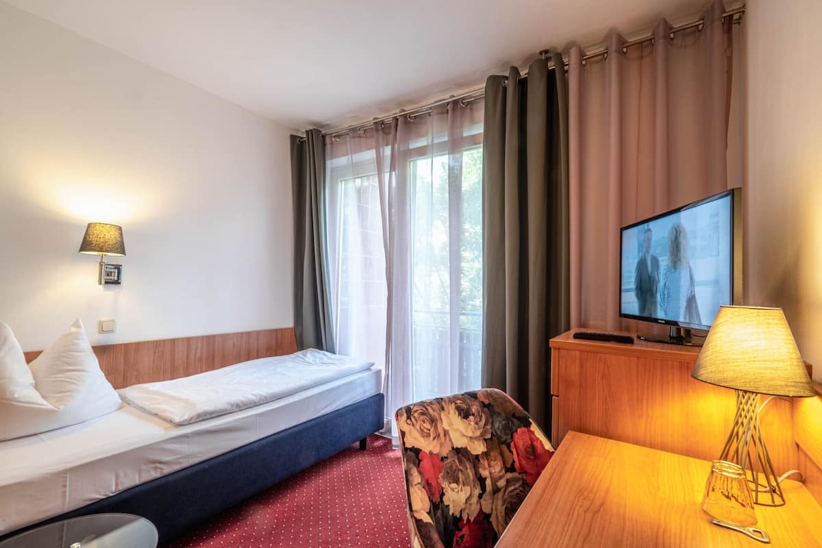 Une chambre d’hôtel avec un lit, un bureau avec une lampe, une télévision et une fenêtre avec des rideaux.