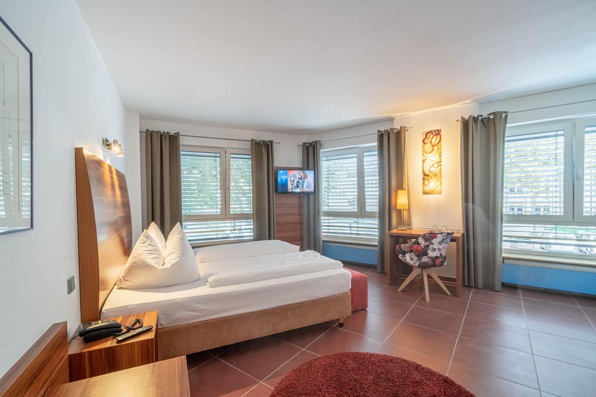 Une chambre d’hôtel avec un lit, une télévision, un bureau avec une lampe et une fenêtre avec des rideaux.