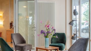 Rebedor modern d'hotel amb un sofà verd, una taula de fusta amb un ram de flors i una porta de vidre que dona a l'exterior.