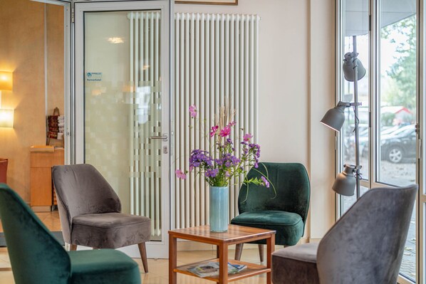 A modern hotel lobby with a green sofa, a wooden table with a vase of flowers, and a glass door leading outside. - Hotel Schottenhof - Cityhotel Mainz (Mainz)