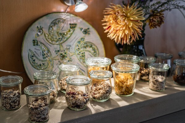 Una exposición de frascos de vidrio llenos de diferentes granos y semillas, dispuestos en un estante con un plato decorativo al fondo.